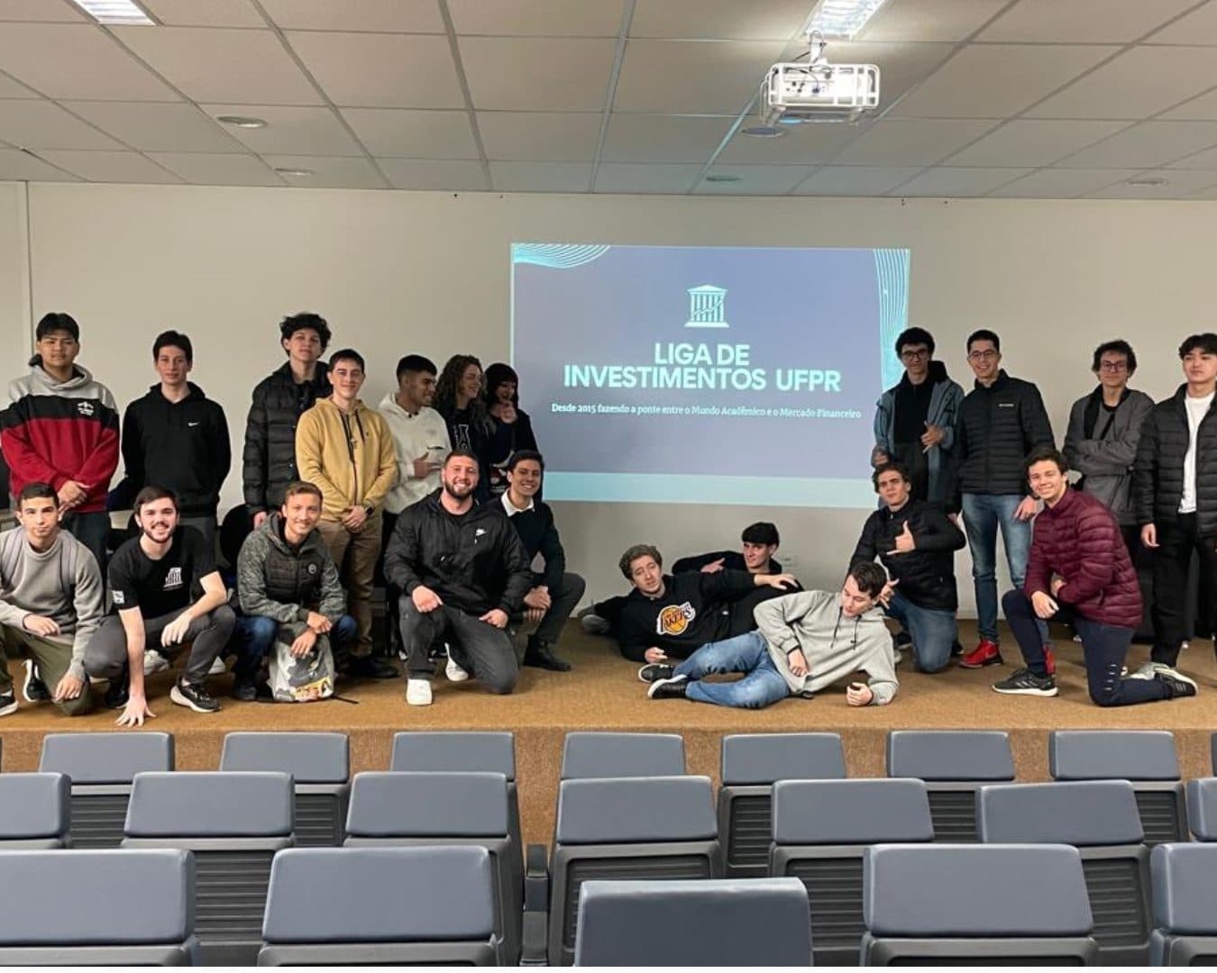 Participantes de um workshop reunidos no palco de um auditório, com o slide da Liga de Investimentos UFPR